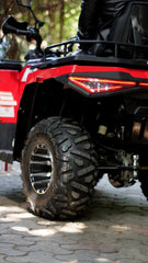 Close-up of a red and black ATV on a paved surface with trees in the background.